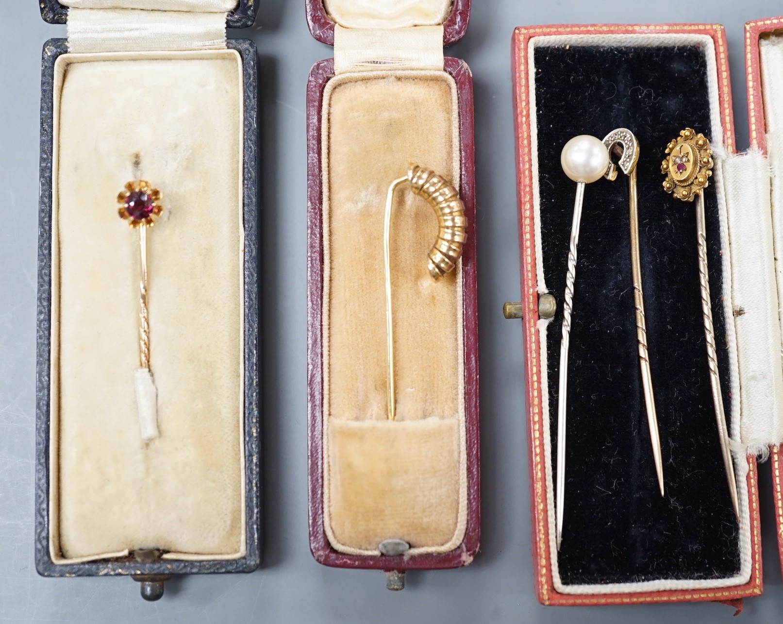 Three assorted early to mid 20th century yellow metal and gem set stick pins including diamond chip set horseshoe, 57mm and 15ct ruby and diamond chip and two other stick pins.